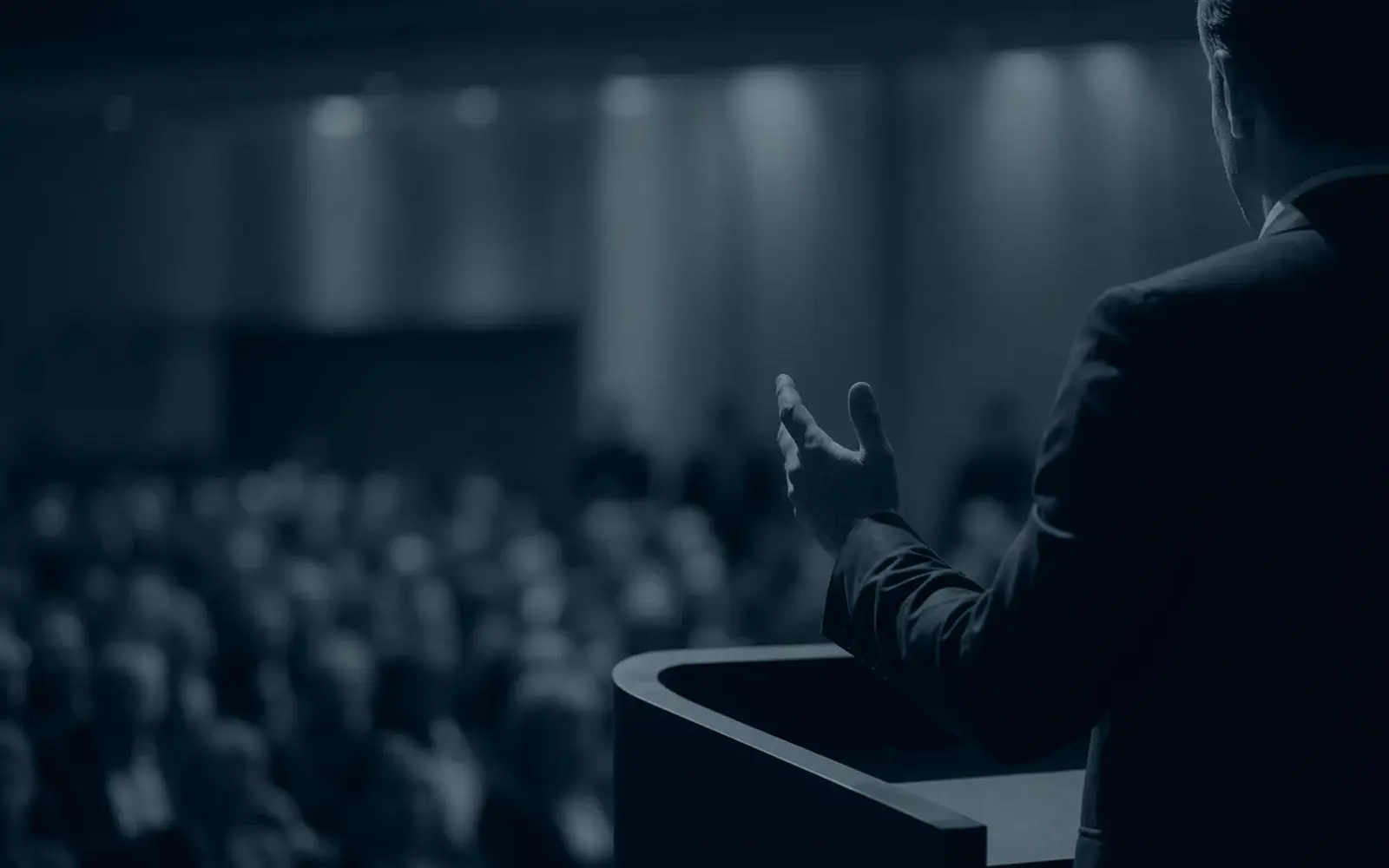 Speaker facing an audience beneath a glowing stage display